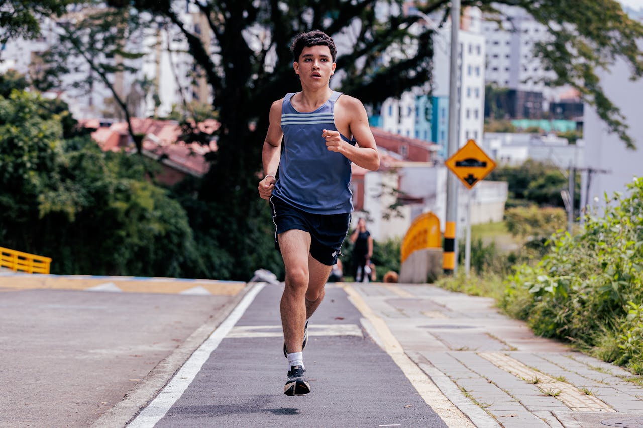 Energetic young man jogging outdoors on a city street surrounded by greenery on a sunny day.